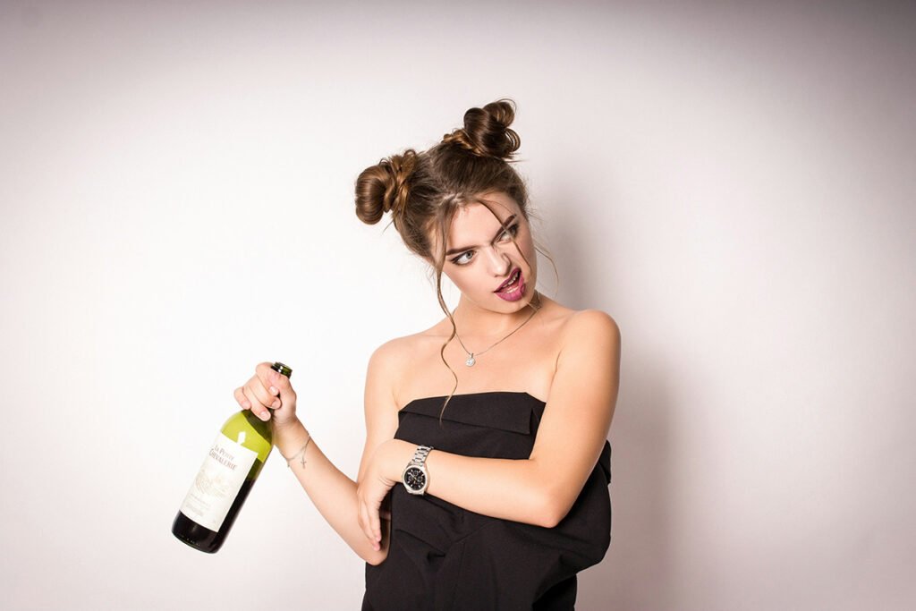 A lady stands wrapped in a towel, holding a bottle of champagne with a silly look on her face...but she's having fun!