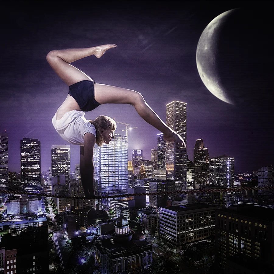 A gymnast does a handstand on a tightrope with a huge moon, and the city of Houston in the background. The prospective of the gymnast on the rope is such that it appears she is balancing over the city.